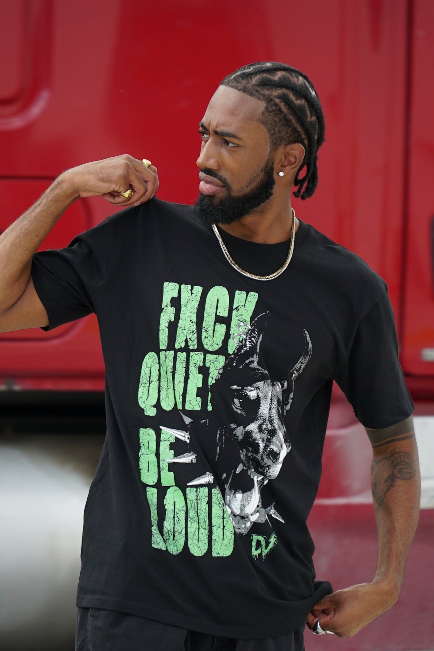 Person wearing a black t-shirt with green text and graphic design, standing in front of a red vehicle.